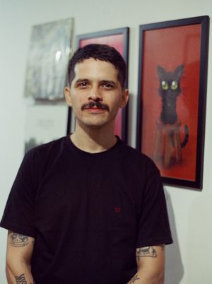Scanned film photograph of a person (a man with short black hair and a mustache wearing a black t-shirt) looking at
            the camera.